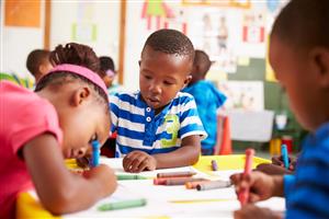 Children sitting at a table, coloring with big crayons.